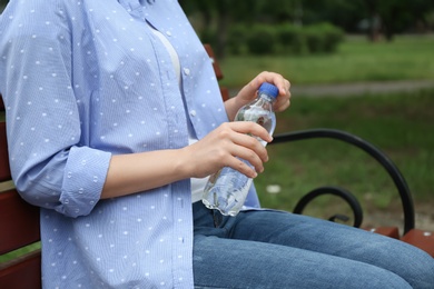 Woman with bottle of water sitting on bench outdoors, closeup
