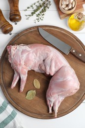Whole raw rabbit, spices and knife at white wooden table, flat lay