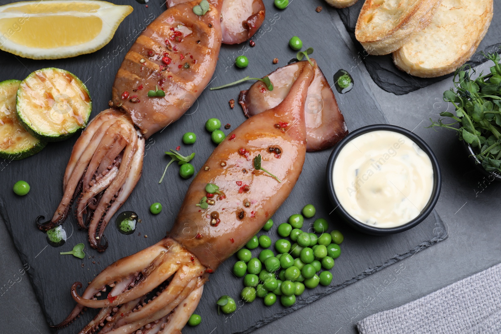 Photo of Tasty grilled squids served on black table, flat lay