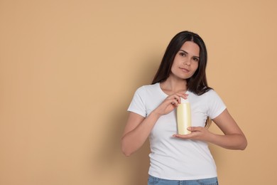 Beautiful young woman holding bottle of shampoo on beige background, space for text