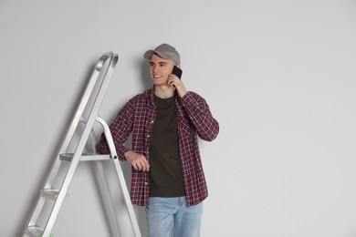Photo of Handyman leaning on stepladder while talking on phone near white wall