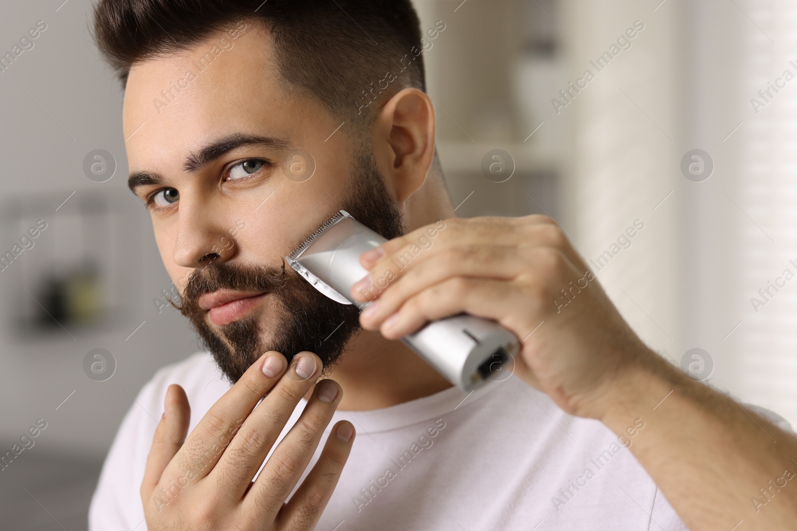 Photo of Handsome young man trimming beard at home