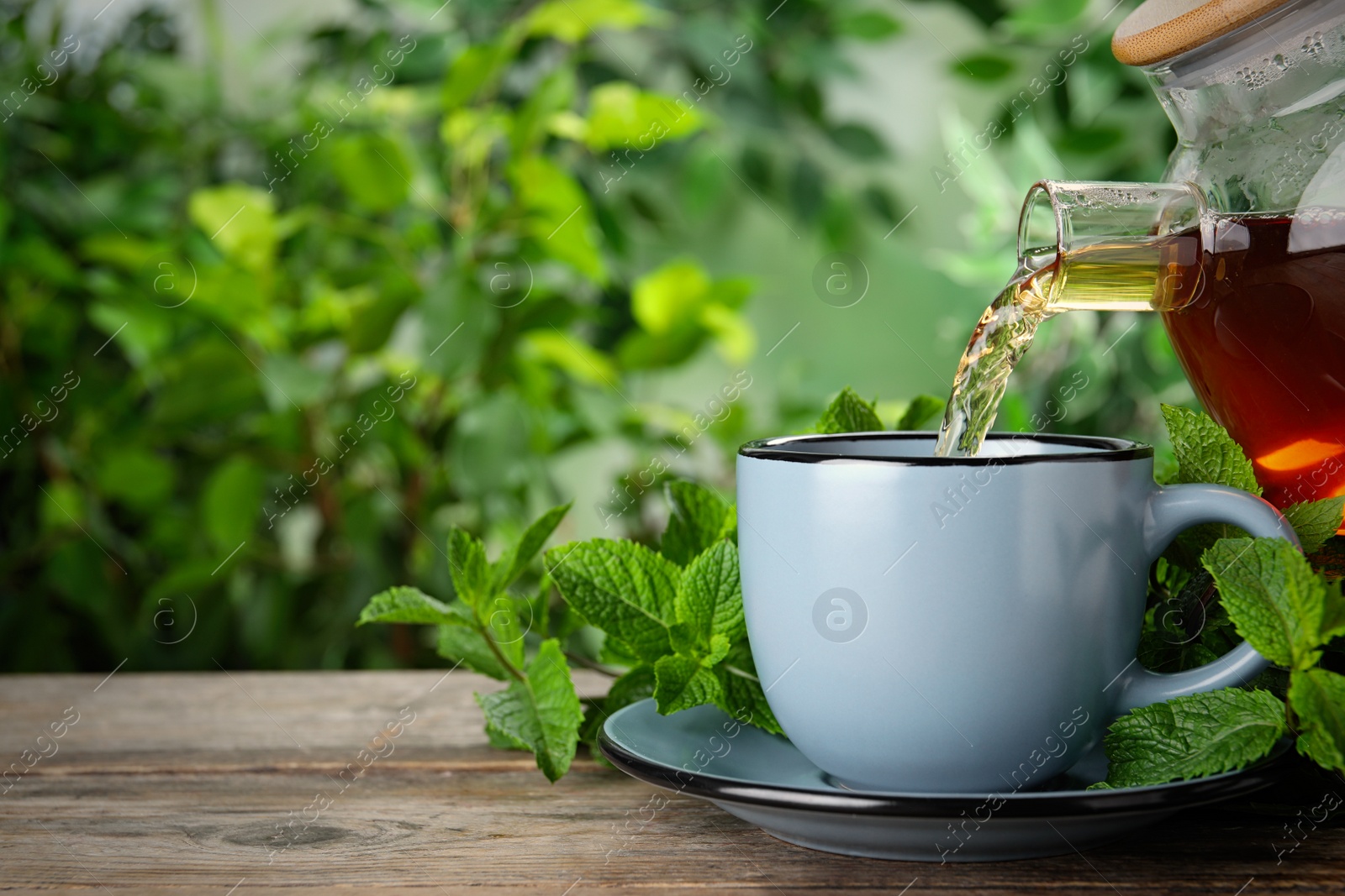 Photo of Pouring fresh mint tea into cup on wooden table, closeup. Space for text