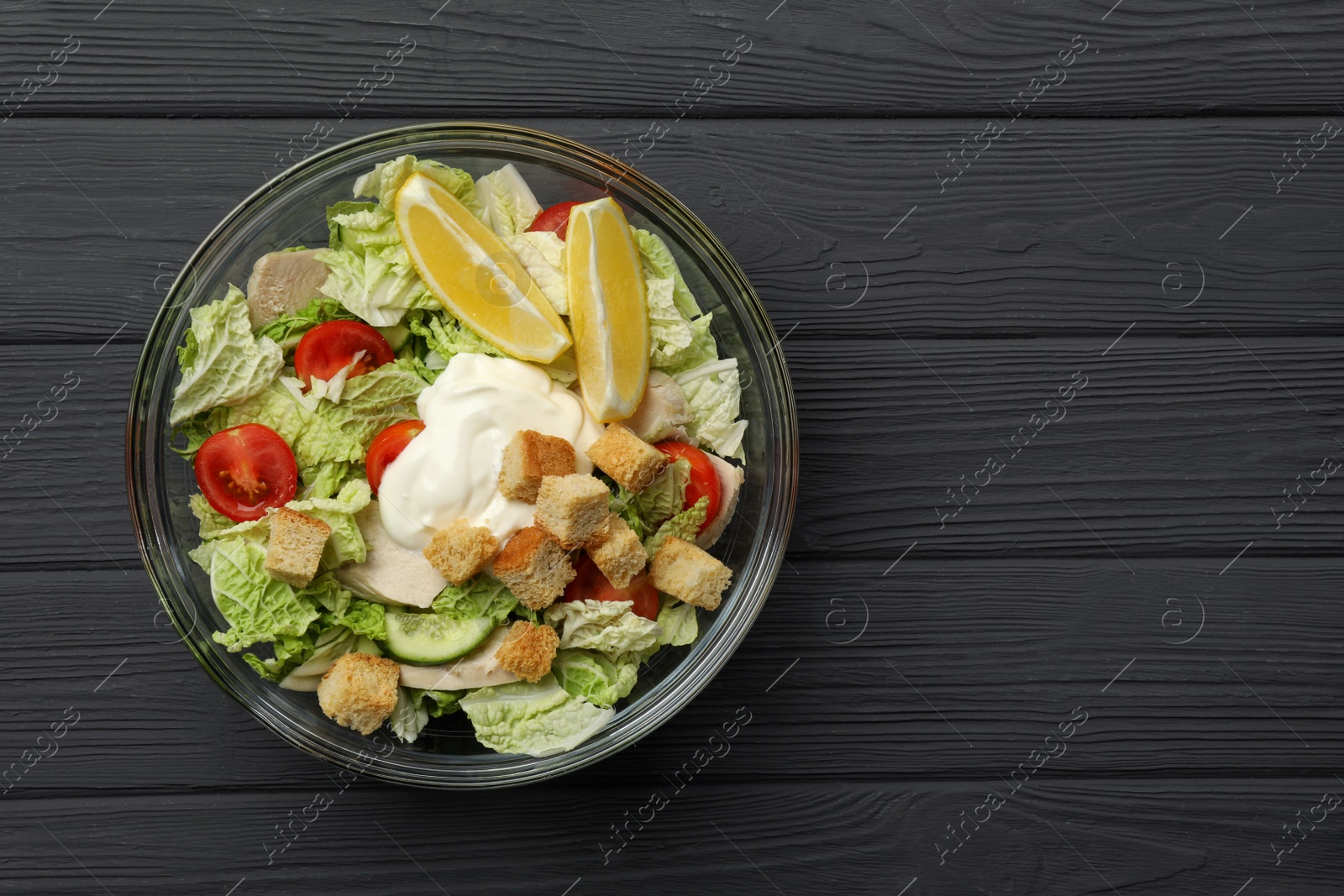 Photo of Bowl of delicious salad with Chinese cabbage, tomatoes and bread croutons on black wooden table, top view. Space for text