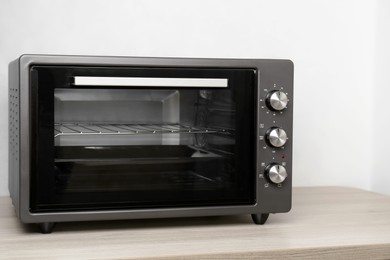 Photo of One electric oven on wooden table near white wall. Space for text