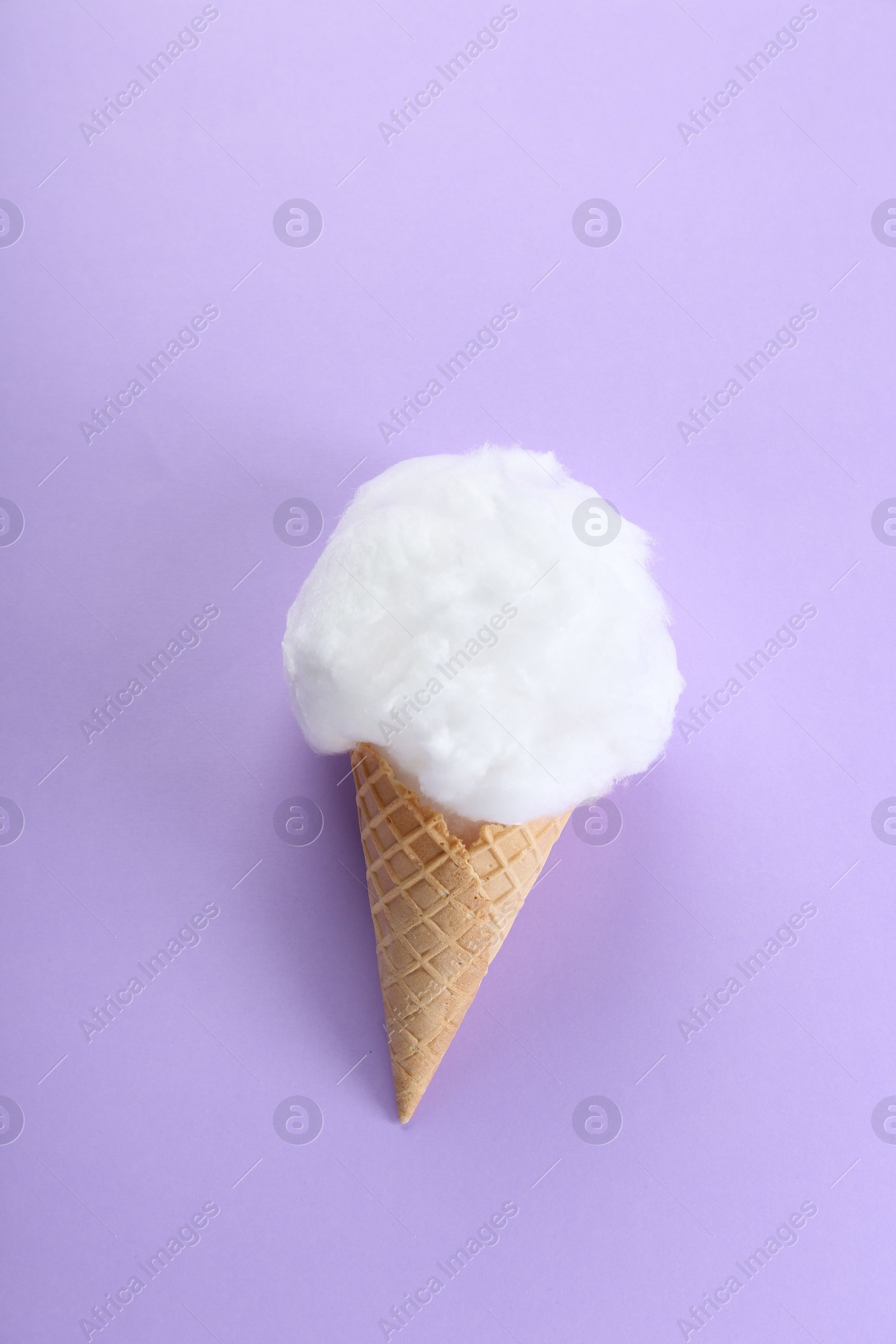 Photo of Sweet cotton candy in waffle cone on purple background, top view