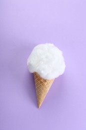 Sweet cotton candy in waffle cone on purple background, top view