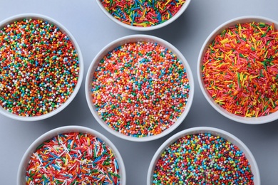 Photo of Colorful sprinkles in bowls on light grey background, flat lay. Confectionery decor