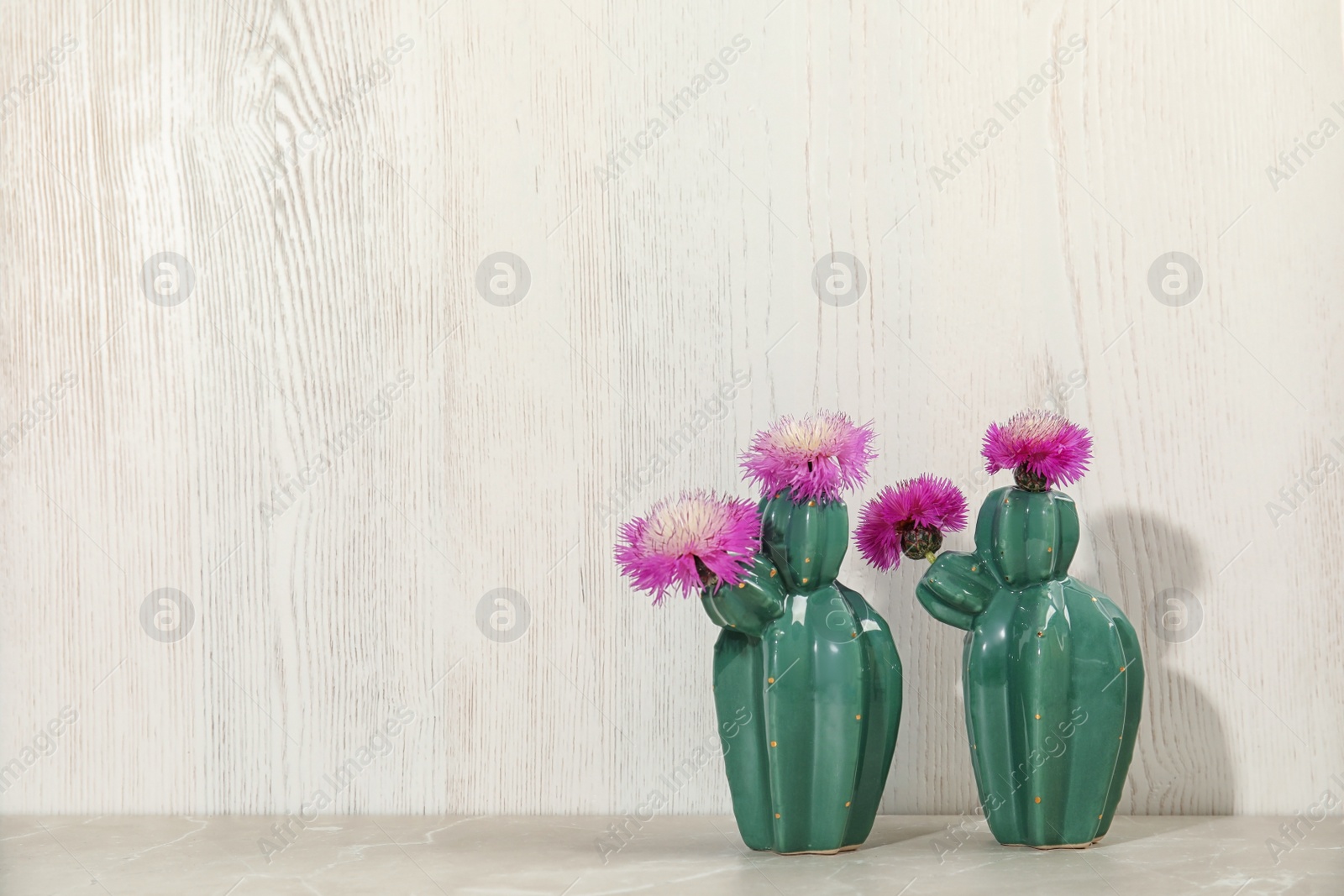 Photo of Trendy cactus shaped ceramic vases with flowers on table against wooden background