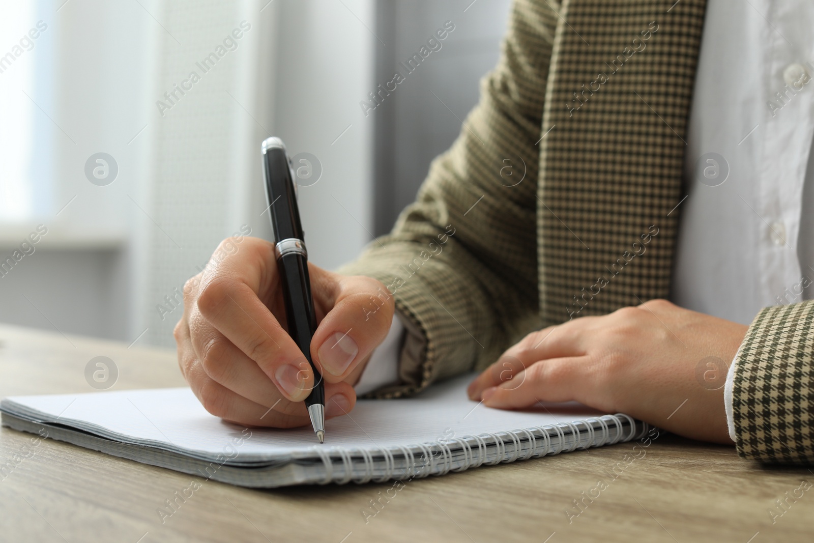 Photo of Woman writing in notebook at wooden table indoors, closeup