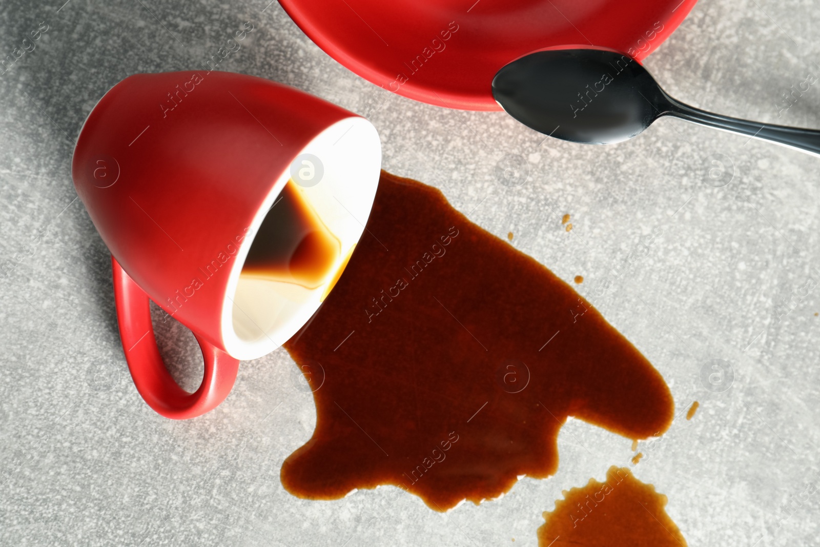 Photo of Cup, saucer and spoon near spilled coffee on grey table