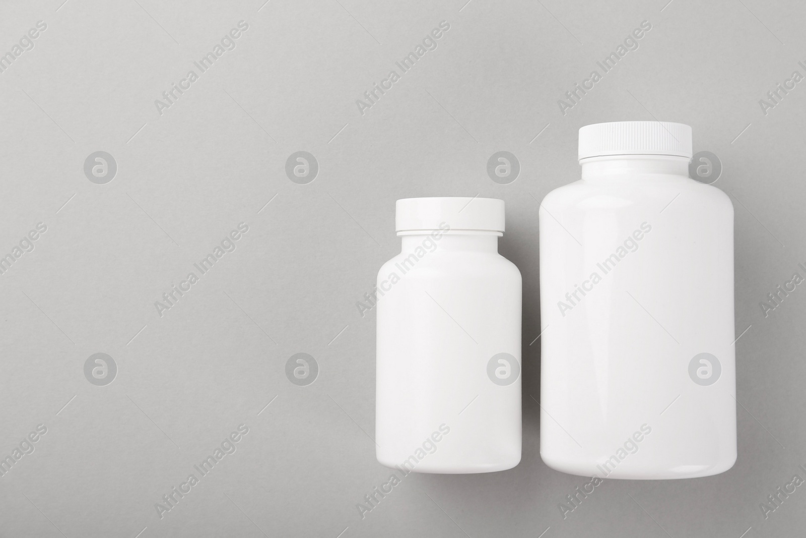 Photo of Blank white pill bottles on light grey background, top view. Space for text