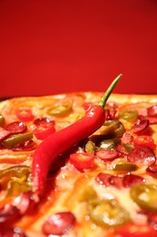 Photo of Delicious pizza Diablo and chili pepper against red background, closeup