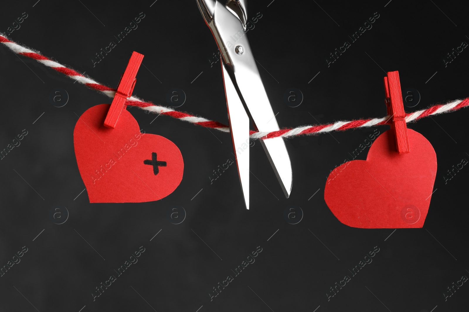 Photo of Red paper hearts on rope and scissors against black background. Composition symbolizing problems in relationship