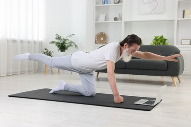 Photo of Senior man in sportswear exercising while watching online tutorial at home
