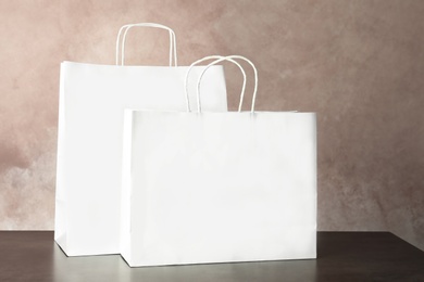 Mockup of paper shopping bags on table against color background