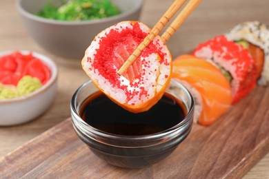 Photo of Holding delicious sushi roll with chopsticks at wooden table, closeup