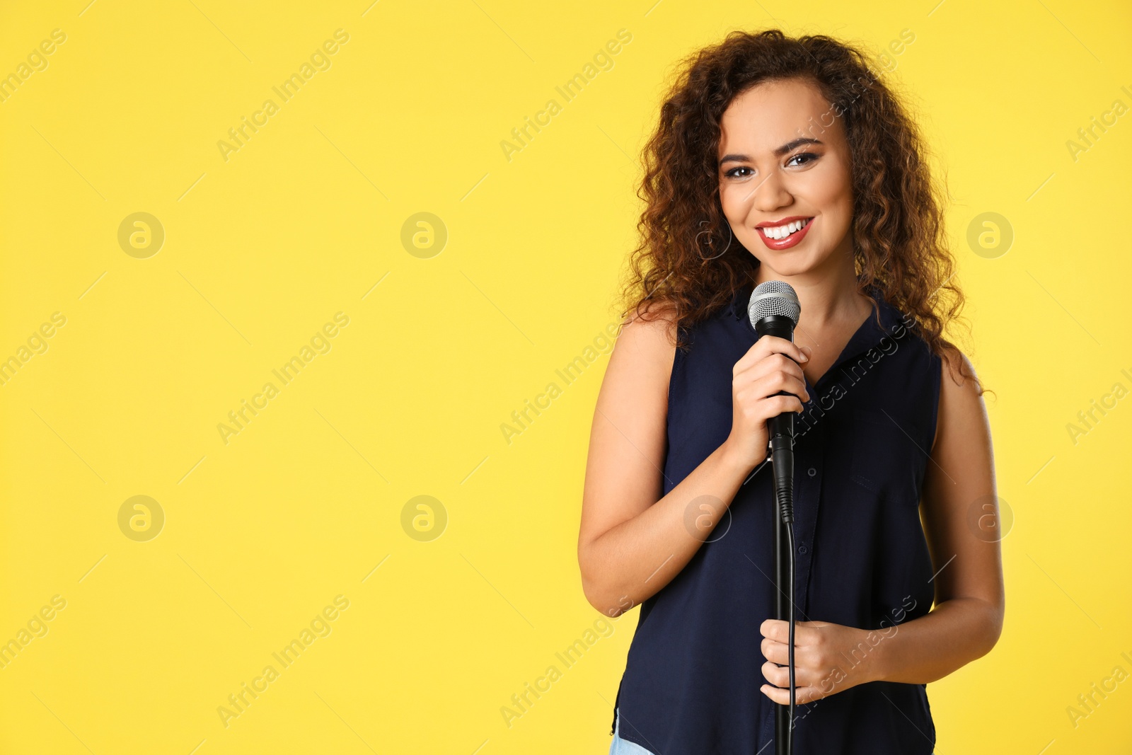 Photo of Portrait of curly African-American woman posing with microphone on color background. Space for text