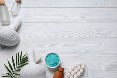 Beautiful spa composition with herbal massage bags and different care products on white wooden table, flat lay. Space for text