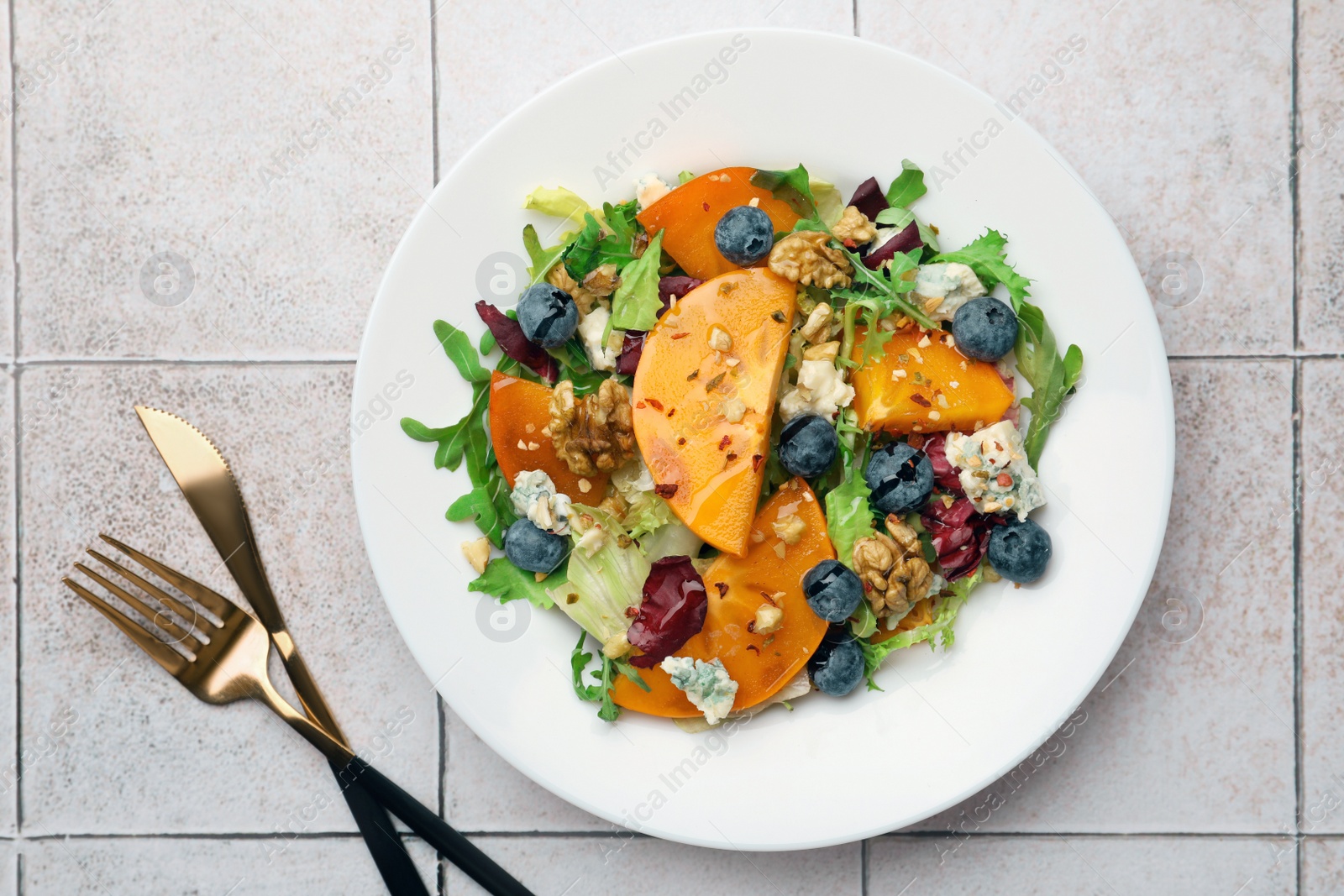 Photo of Delicious persimmon salad, fork and knife on tiled surface, flat lay