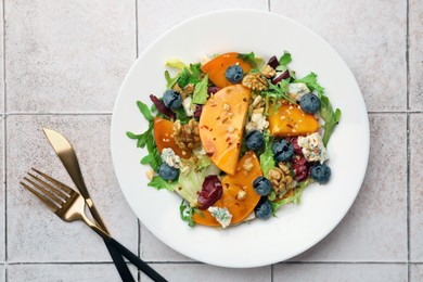 Delicious persimmon salad, fork and knife on tiled surface, flat lay