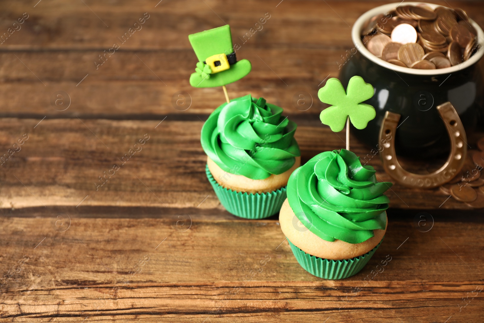 Photo of Decorated cupcakes and pot with gold coins on wooden table. St. Patrick's Day celebration