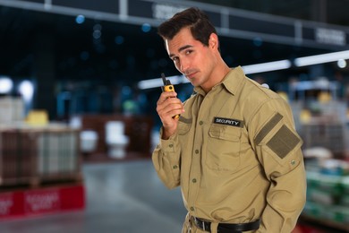 Image of Male security guard wearing uniform using portable radio transmitter in shopping mall