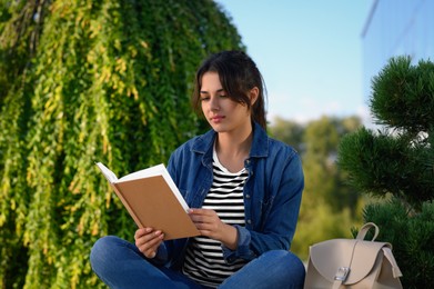 Photo of Young woman reading book outdoors on sunny day