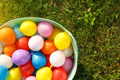 Basin full of water bombs on green grass, top view. Space for text