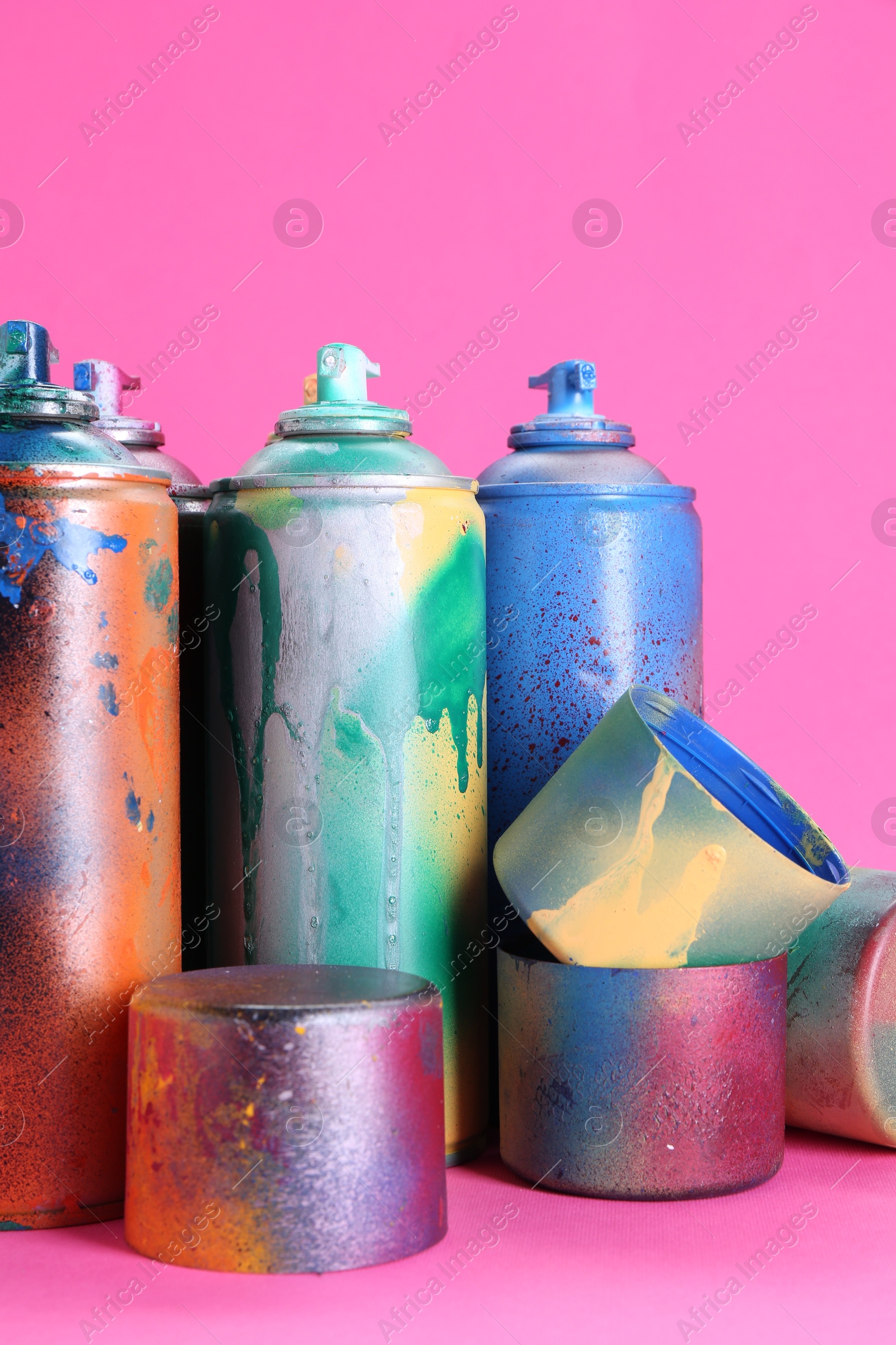 Photo of Many spray paint cans with caps on pink background, closeup