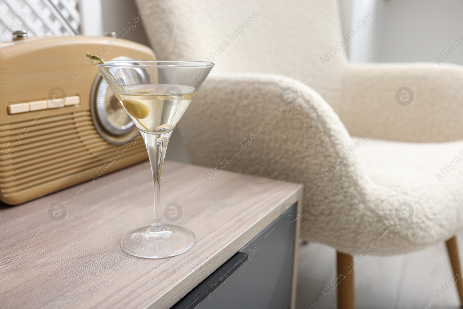 Photo of Martini cocktail with olive and retro radio receiver on wooden table in room, space for text. Relax at home