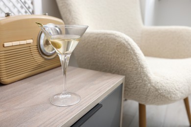 Photo of Martini cocktail with olive and retro radio receiver on wooden table in room, space for text. Relax at home