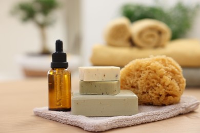 Bottle of essential oil, soap bars and natural sponge on light wooden table, closeup. Spa therapy