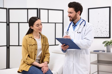 Photo of Doctor with clipboard consulting patient during appointment in clinic