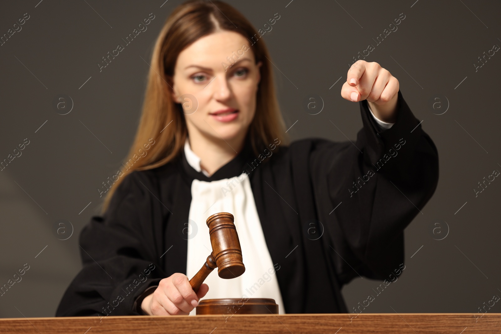 Photo of Judge striking mallet at wooden table in courtroom, selective focus