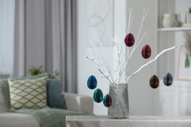 Photo of Branches with paper eggs in vase on table indoors, space for text. Beautiful Easter decor.
