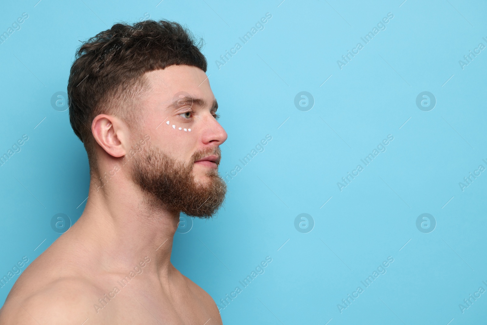 Photo of Handsome man with moisturizing cream on his face against light blue background, space for text