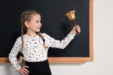 Pupil with school bell near black chalkboard in classroom
