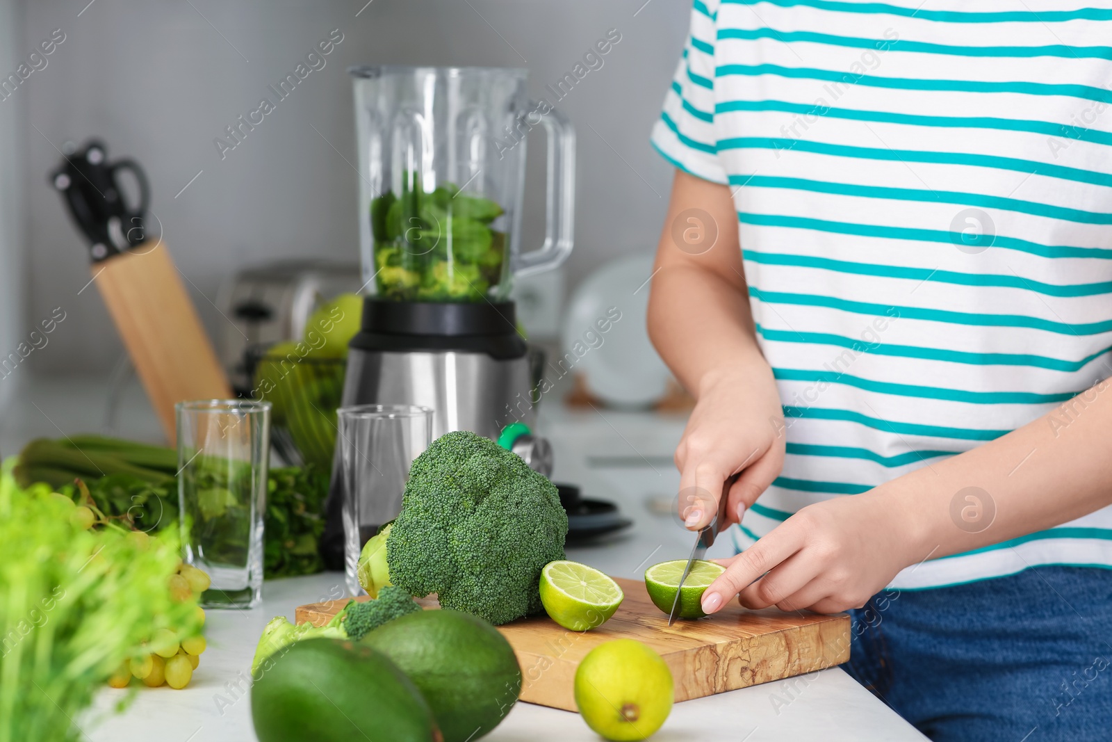 Photo of Woman cutting lime for smoothie in kitchen, closeup