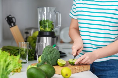 Woman cutting lime for smoothie in kitchen, closeup