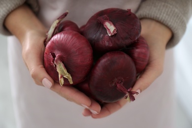 Woman holding red onions on blurred background, closeup