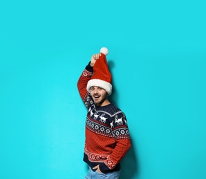 Photo of Young man in Christmas sweater and hat on color background