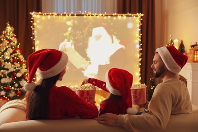 Photo of Family watching movie on projection screen in room decorated for Christmas, back view. Home TV equipment