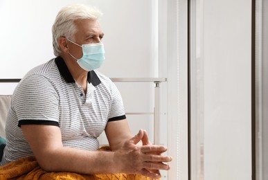 Senior man with protective mask resting in armchair at nursing home