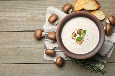 Tasty homemade mushroom soup in ceramic pot, croutons, fresh champignons and rosemary on wooden table, flat lay. Space for text