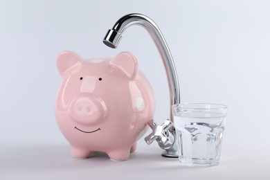 Photo of Water scarcity concept. Piggy bank, tap and glass of drink isolated on white