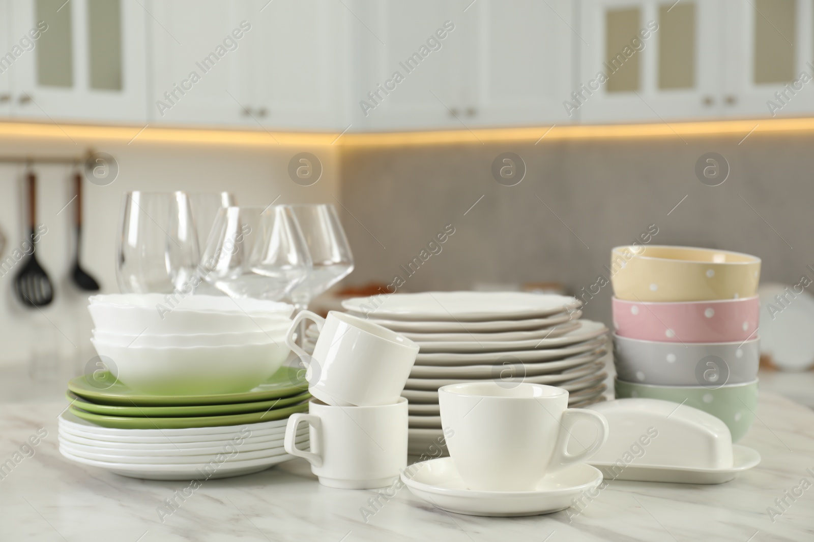 Photo of Clean plates, bowls, cups and glasses on white marble table in kitchen