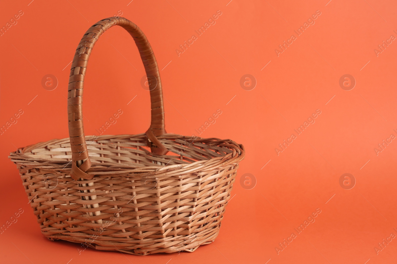 Photo of Empty wicker basket on coral background, space for text. Easter item