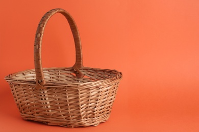 Photo of Empty wicker basket on coral background, space for text. Easter item