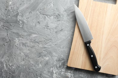 Knife and wooden board on grey textured table, top view. Space for text